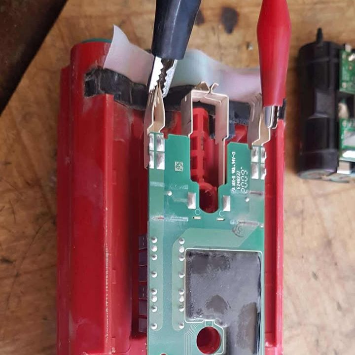 O placă de circuit cu cleme crocodil roșii și negre atașate, așezată pe un acumulator.
