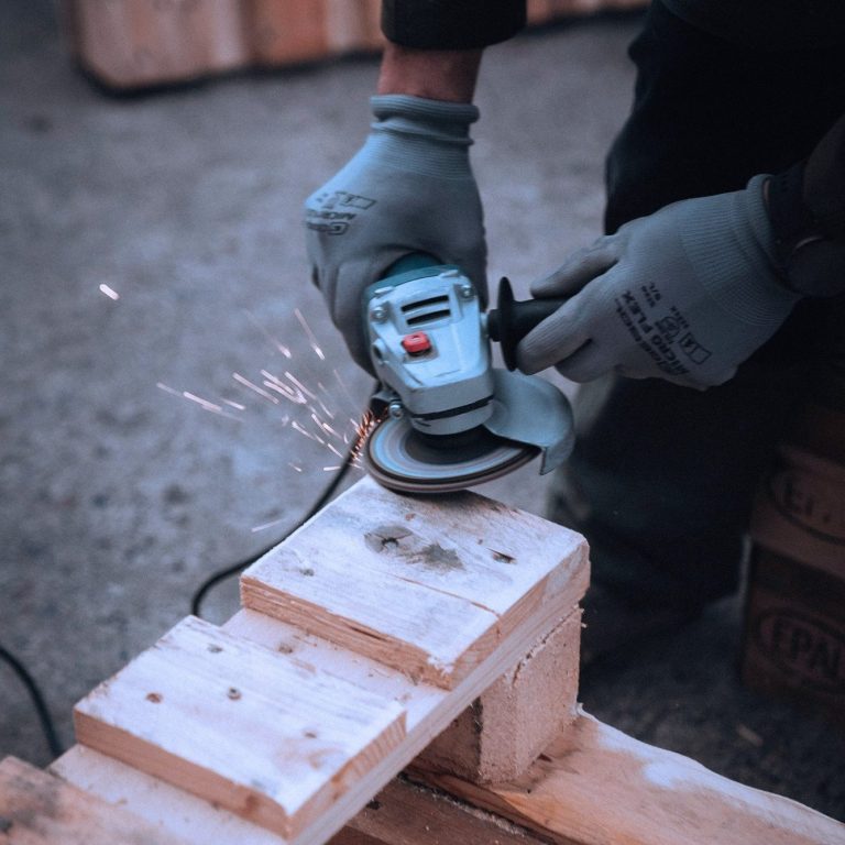 O persoană folosește o unealtă electrică pentru a șlefui lemn, iar scântei zboară de pe suprafață.