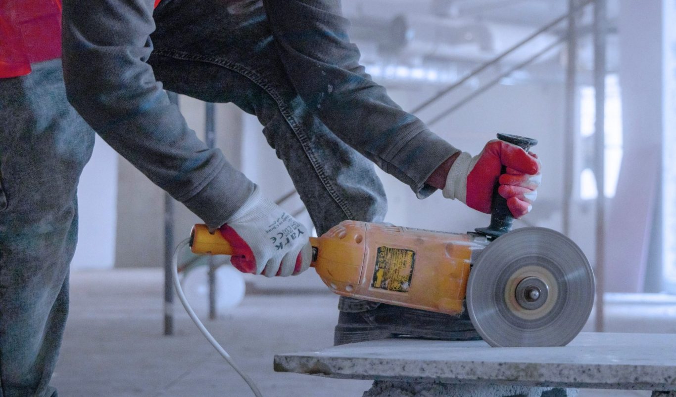 Un muncitor folosește o unealtă electrică pentru a tăia material într-un șantier de construcții.
